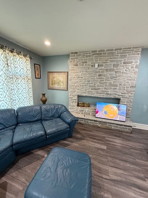 living room with a stone fireplace and dark hardwood / wood-style flooring