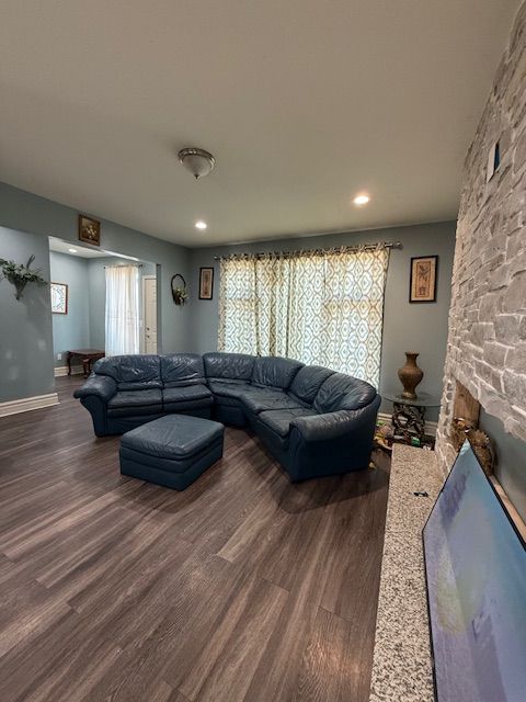 living room featuring a stone fireplace and dark wood-type flooring