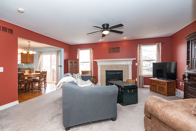 carpeted living room featuring a tile fireplace, a wealth of natural light, and ceiling fan with notable chandelier