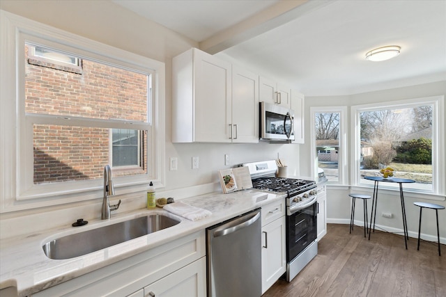 kitchen with white cabinetry, stainless steel appliances, sink, and light stone counters