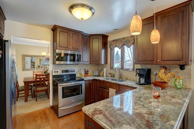 kitchen featuring sink, appliances with stainless steel finishes, hanging light fixtures, decorative backsplash, and light wood-type flooring