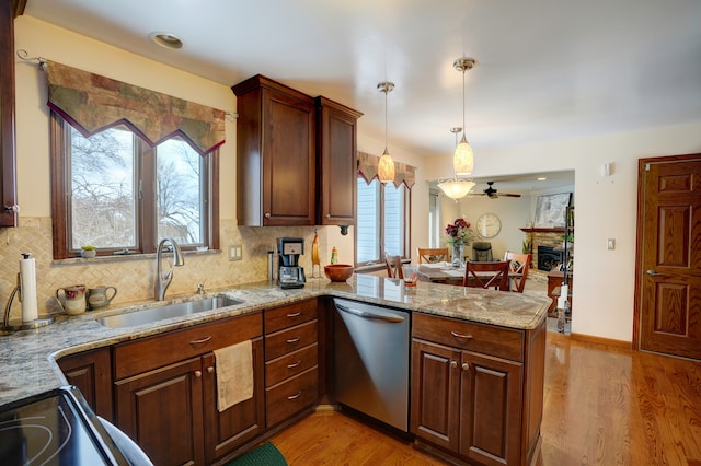 kitchen with sink, light stone counters, decorative light fixtures, stainless steel dishwasher, and kitchen peninsula