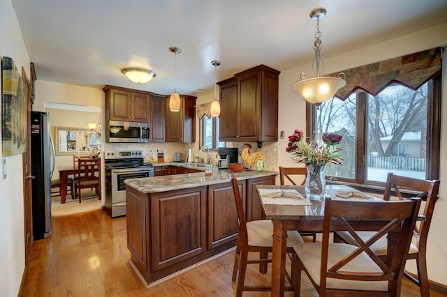 kitchen featuring appliances with stainless steel finishes, light stone countertops, decorative backsplash, decorative light fixtures, and kitchen peninsula