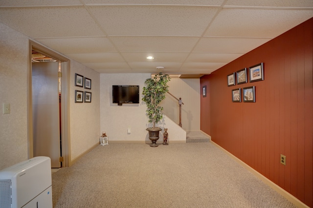 basement with carpet flooring, a paneled ceiling, and wooden walls