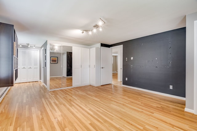 unfurnished bedroom featuring multiple closets, rail lighting, and light hardwood / wood-style floors