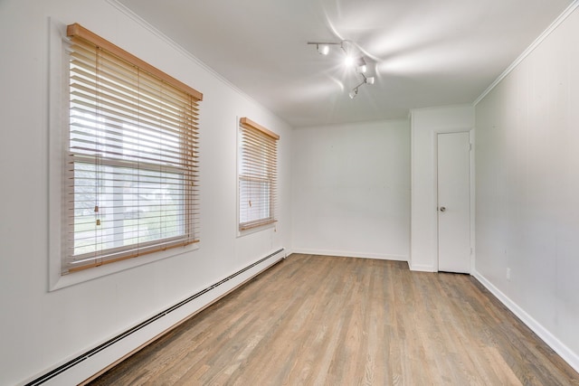 empty room featuring a baseboard heating unit, light hardwood / wood-style flooring, ornamental molding, and rail lighting