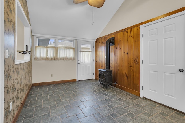 entryway with ceiling fan, lofted ceiling, wooden walls, and a wood stove