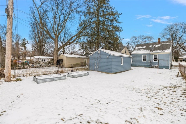 snow covered property with a garage, an outbuilding, and fence