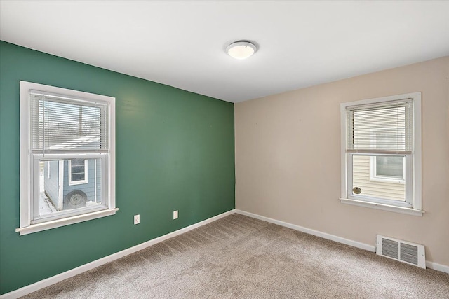 carpeted spare room featuring baseboards, visible vents, and a healthy amount of sunlight