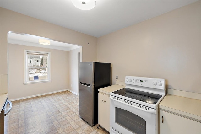 kitchen with electric stove, light countertops, freestanding refrigerator, and baseboards