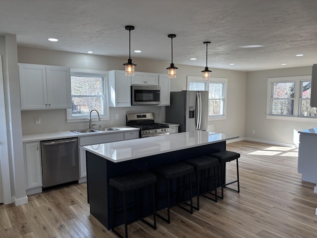 kitchen with sink, stainless steel appliances, white cabinets, a kitchen island, and decorative light fixtures