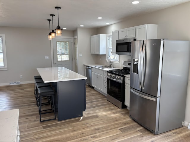 kitchen featuring appliances with stainless steel finishes, decorative light fixtures, sink, white cabinets, and a center island