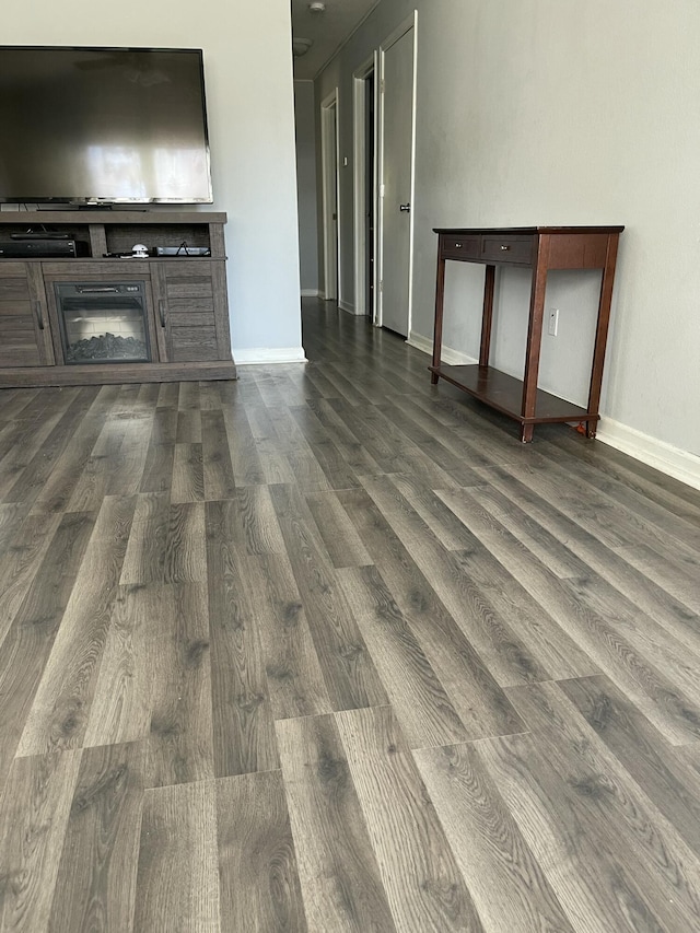 unfurnished living room with baseboards, dark wood-type flooring, and a glass covered fireplace