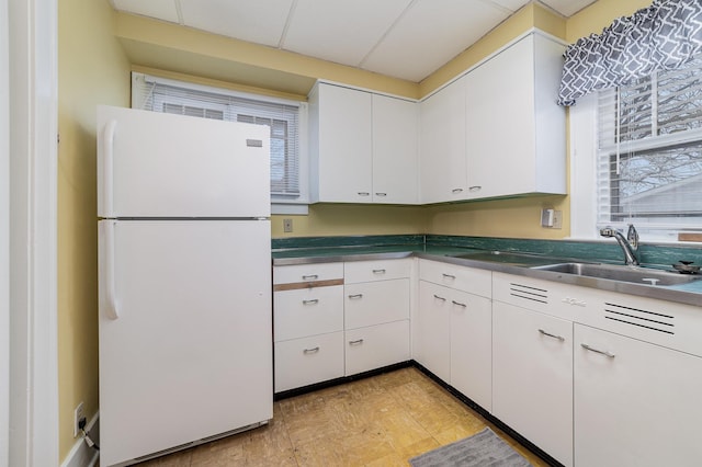 kitchen with white refrigerator, white cabinetry, and sink