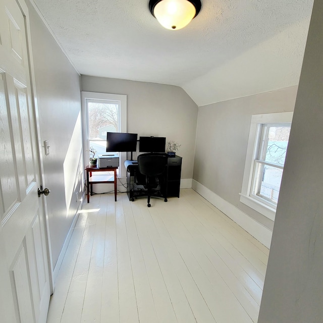 office area featuring light hardwood / wood-style floors, vaulted ceiling, and a textured ceiling