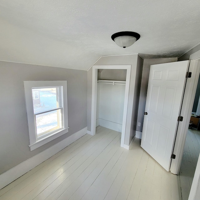 unfurnished bedroom with a closet, vaulted ceiling, a textured ceiling, and light wood-type flooring