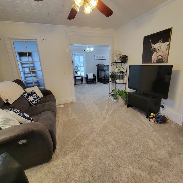 living room with a fireplace, crown molding, ceiling fan with notable chandelier, and carpet flooring