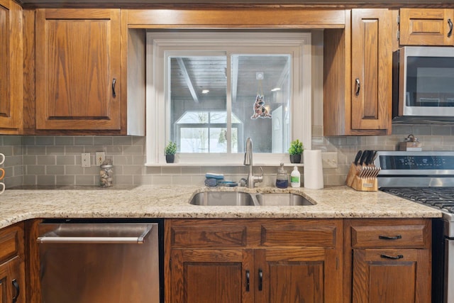 kitchen featuring appliances with stainless steel finishes, light stone countertops, sink, and backsplash