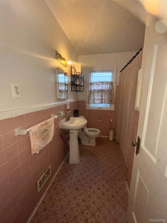 bathroom featuring toilet, sink, vaulted ceiling, tile walls, and curtained shower