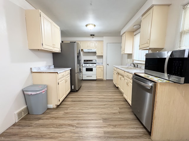 kitchen featuring sink, cream cabinets, light hardwood / wood-style flooring, and appliances with stainless steel finishes