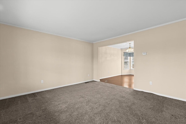 spare room with ornamental molding, a chandelier, and dark colored carpet