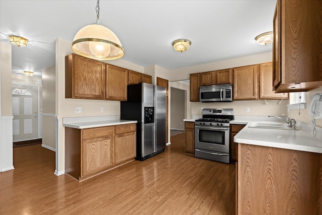 kitchen with stainless steel appliances, sink, pendant lighting, and light hardwood / wood-style floors