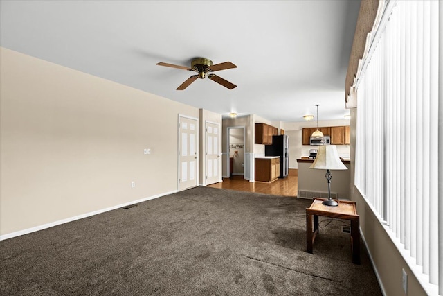 unfurnished living room with ceiling fan and dark colored carpet