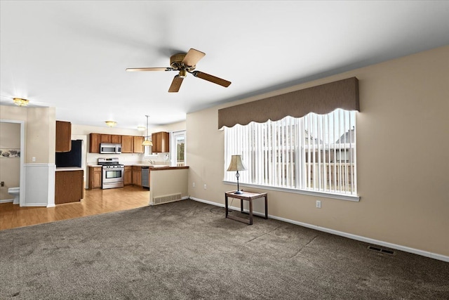 unfurnished living room with ceiling fan, light colored carpet, and sink