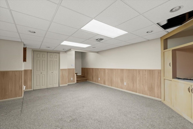 basement featuring a paneled ceiling, light colored carpet, and wood walls