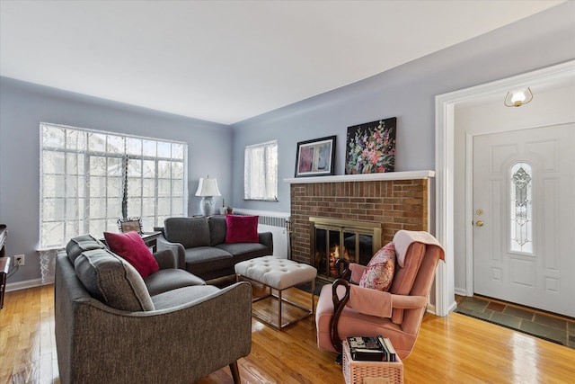 living room with wood-type flooring, a brick fireplace, and radiator heating unit