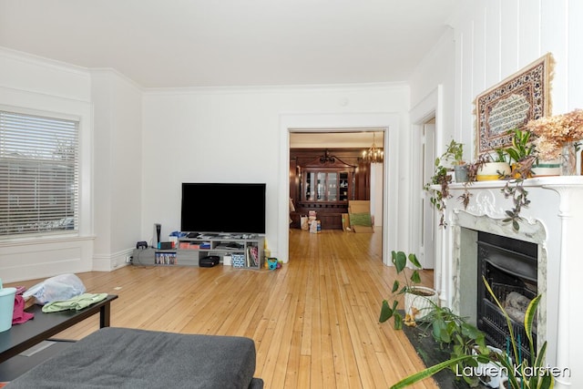 living room with wood-type flooring, crown molding, a notable chandelier, and a high end fireplace