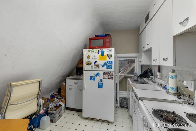 kitchen featuring vaulted ceiling, white fridge, and white cabinets