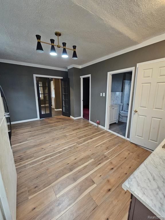 unfurnished bedroom with french doors, connected bathroom, a textured ceiling, ornamental molding, and hardwood / wood-style flooring