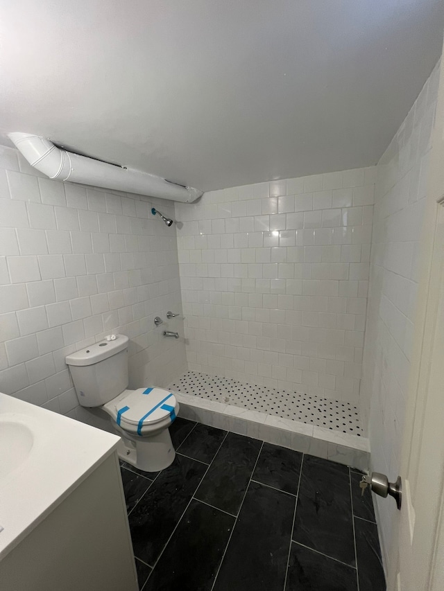 bathroom featuring tile walls, tiled shower, vanity, tile patterned floors, and toilet