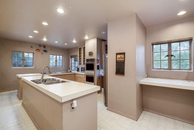 kitchen featuring a large island with sink, sink, white double oven, and kitchen peninsula