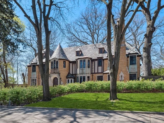 english style home with brick siding, a front lawn, and fence