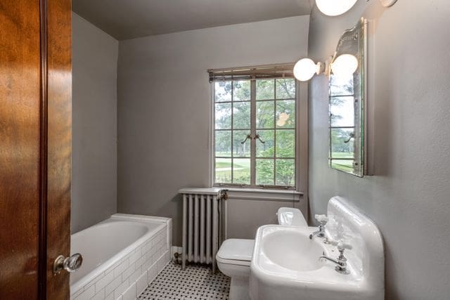 bathroom featuring toilet, sink, radiator heating unit, and a relaxing tiled tub