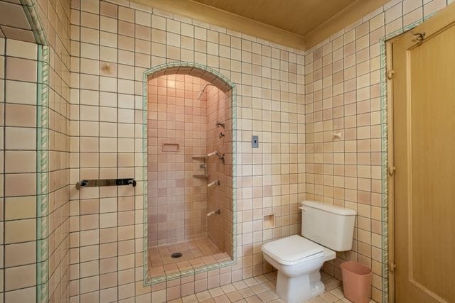 bathroom with tile walls, a tile shower, ornamental molding, tile patterned floors, and toilet