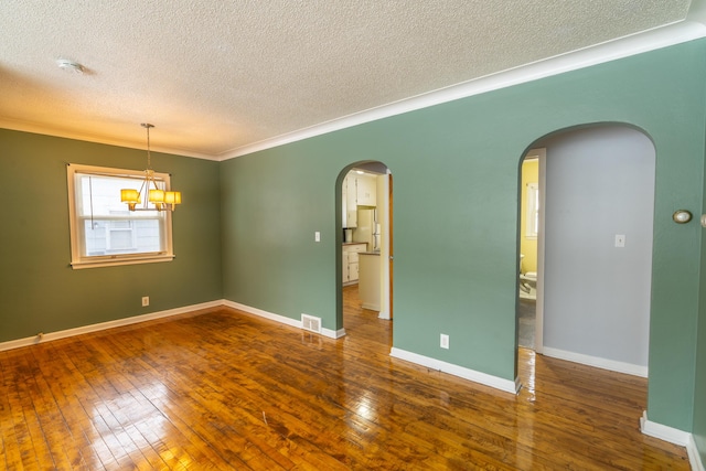 spare room featuring a notable chandelier, dark wood-type flooring, ornamental molding, and a textured ceiling