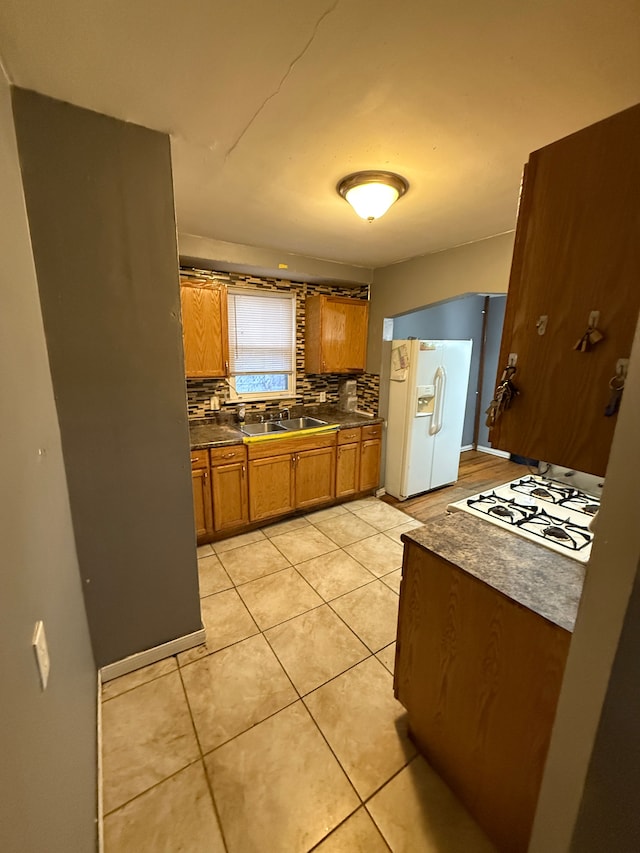 kitchen featuring sink, light tile patterned floors, gas cooktop, tasteful backsplash, and white fridge with ice dispenser