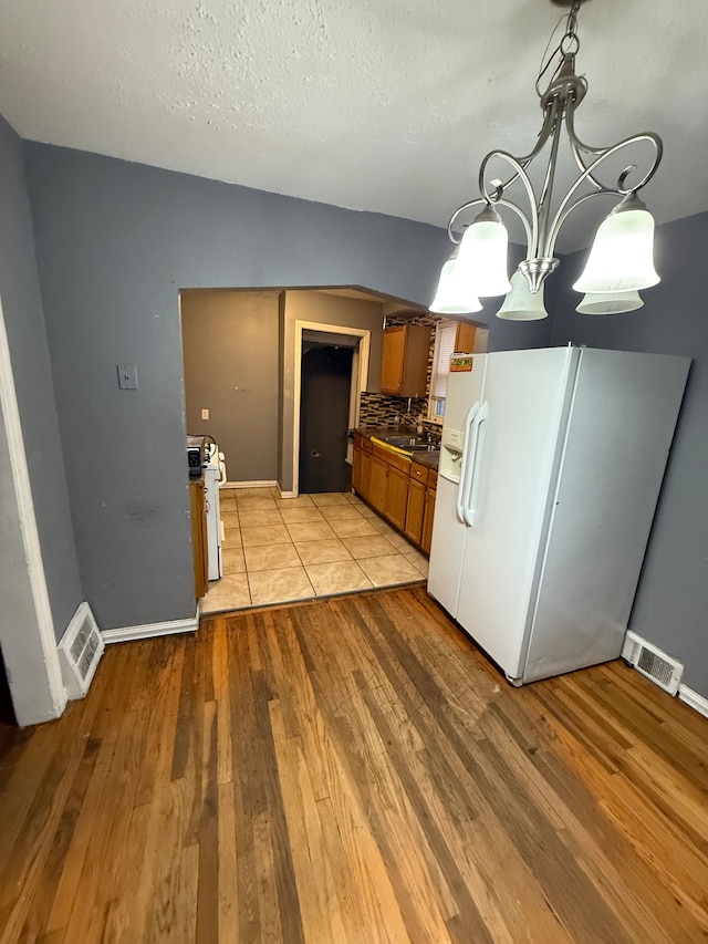 kitchen with white appliances, a notable chandelier, a textured ceiling, decorative backsplash, and light wood-type flooring