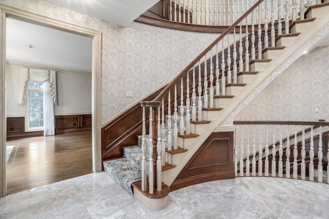 staircase with a wainscoted wall, wallpapered walls, and wood finished floors