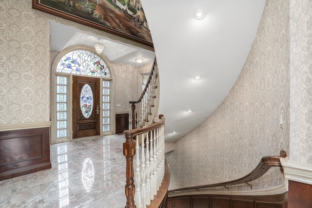 foyer featuring wainscoting, wallpapered walls, marble finish floor, and stairs