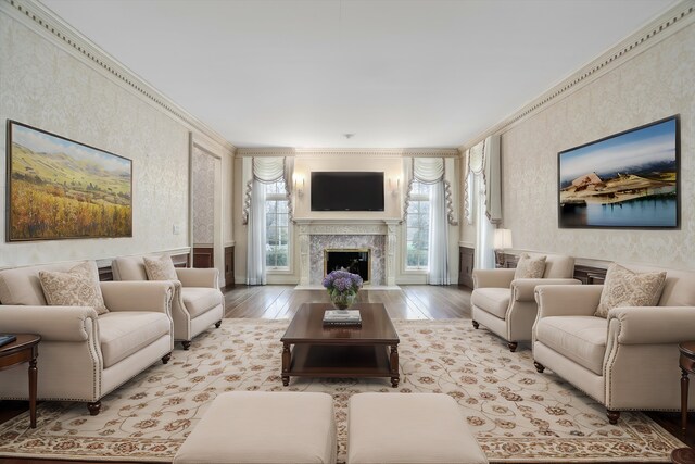 living room featuring light wood-style floors, ornamental molding, a fireplace, and wallpapered walls