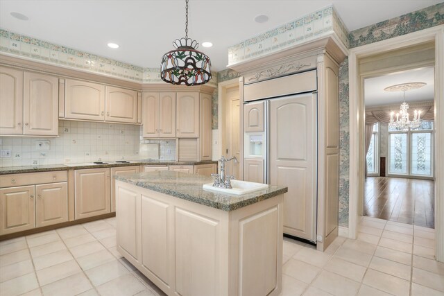 kitchen featuring a sink, backsplash, a kitchen island, light stone countertops, and white cooktop