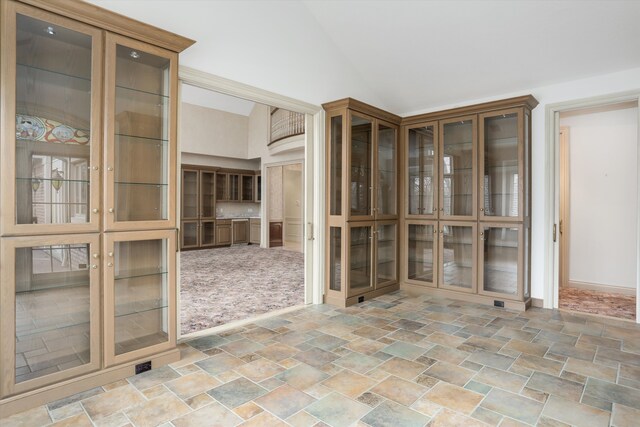 carpeted empty room featuring french doors, high vaulted ceiling, stone finish flooring, and baseboards