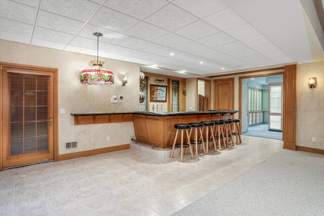 bar featuring visible vents, baseboards, indoor wet bar, a paneled ceiling, and decorative light fixtures