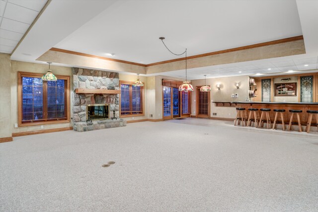 unfurnished living room with baseboards, a tray ceiling, carpet floors, a stone fireplace, and a bar