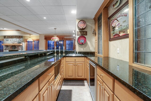 kitchen featuring a sink, dark stone countertops, light tile patterned flooring, a paneled ceiling, and hanging light fixtures