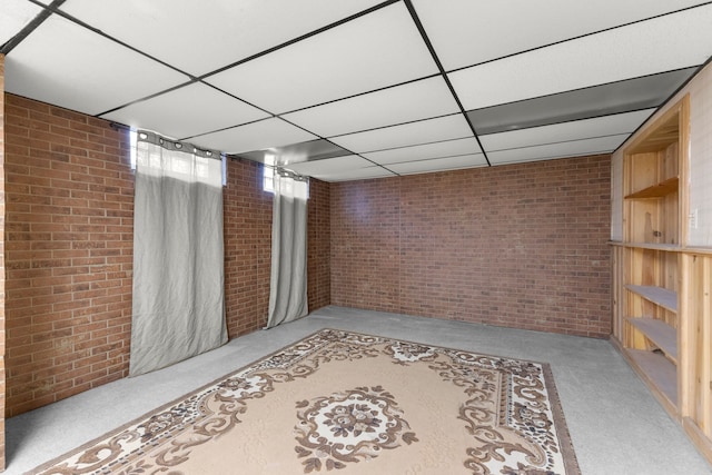 basement with brick wall, a paneled ceiling, and light colored carpet